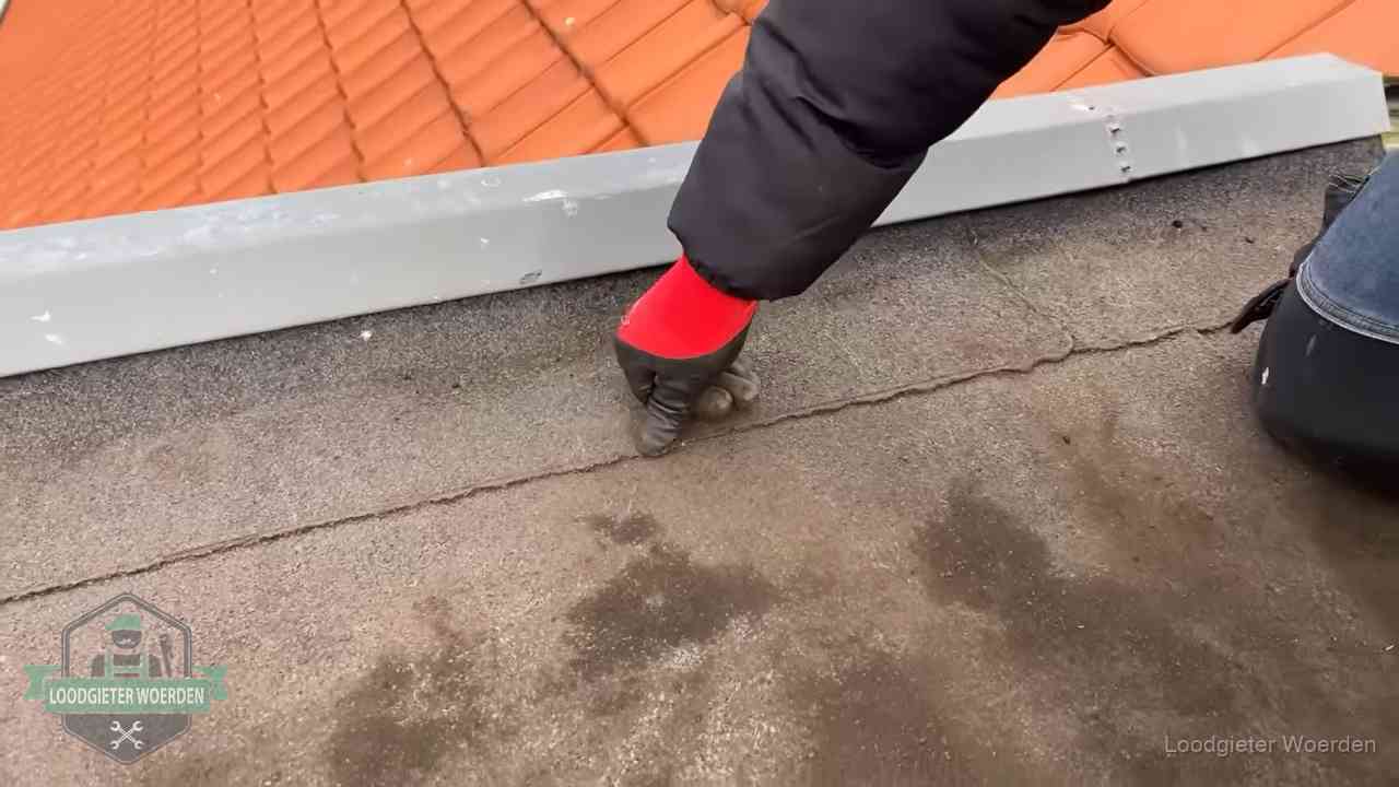 Vakman wijst een naad met vochtplekken aan op een bitumen plat dak in Woerden