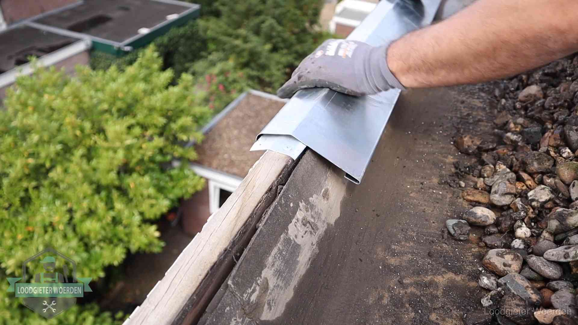 Dakdekker plaatst een zinken deklijst op een dakrand met uitzicht over een woonwijk in Woerden