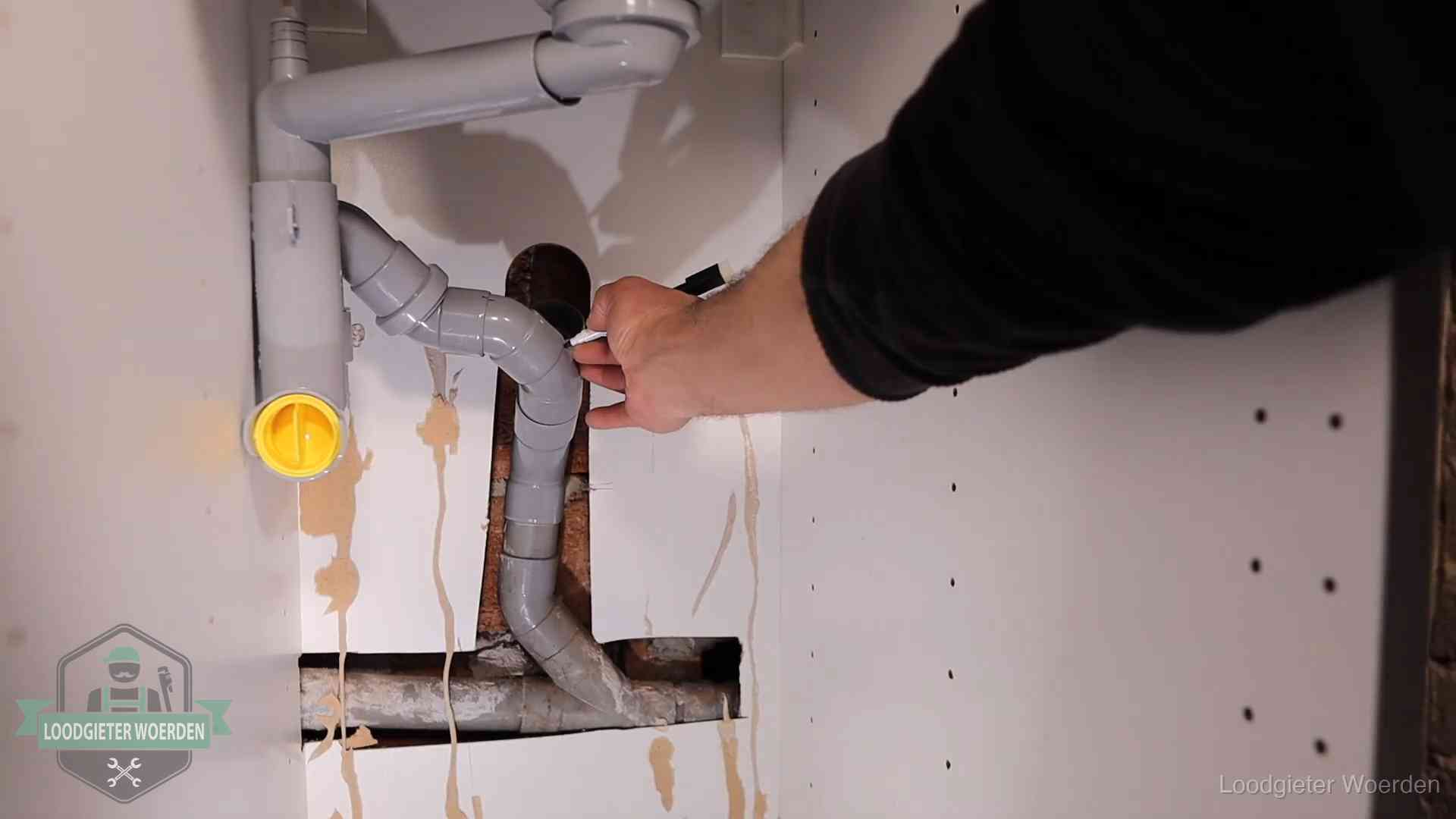 Loodgieter voor verhuurders en bedrijven in Woerden Loodgieter markeert een pvc-afvoerbuis onder een gootsteen in Woerden