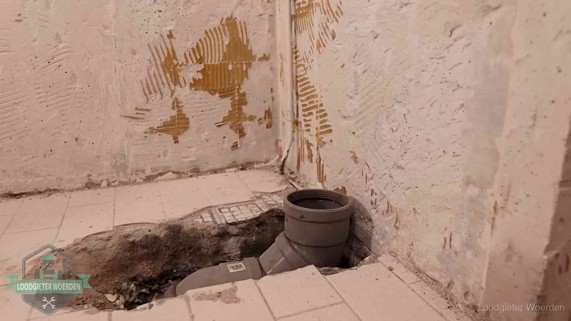 Verzakt riool herstellen in Woerden Opengebroken vloer met een nieuwe pvc-rioolbocht in een gegraven sleuf in Woerden
