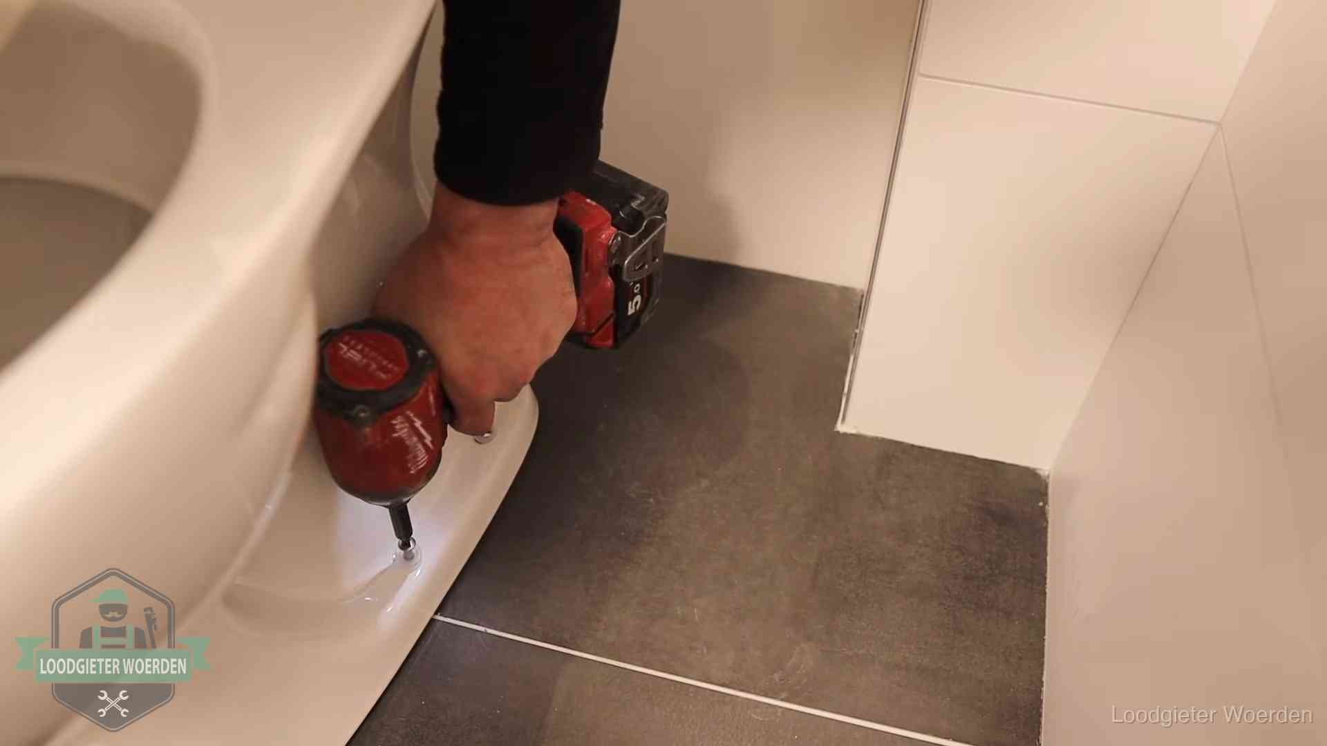 Kosten wc ontstoppen in Woerden Loodgieter zet de voet van een wc-pot vast op de tegelvloer in Woerden